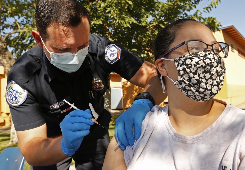 Diana Gomez receives a Pfizer COVID vaccine shot at a charter school in Arleta from Kyle Carson, an EMT.
