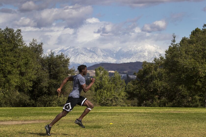 FULLERTON, CA - January 25: A runner has a little help from gusty winds while exercising with a view of snow-capped San Gabriel Mountains courtesy of a series of storms to hit Southern California at Hillcrest Park in Fullerton Monday, Jan. 25, 2021. (Allen J. Schaben / Los Angeles Times)