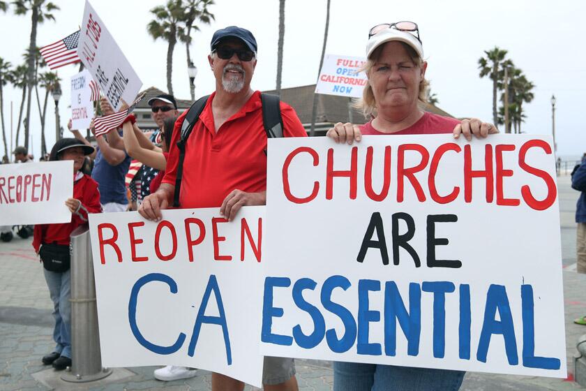 Wally Thomas of Lake Forest and Denean MacAndrew of Mission Viejo take part in a protest in Huntington Beach on May 9, 2020.