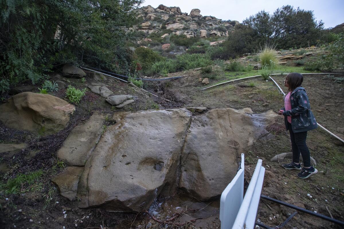 Maleeyah Rivas looks up at the hill behind her family's modular home in West Hills that was damaged in a mudslide last week.