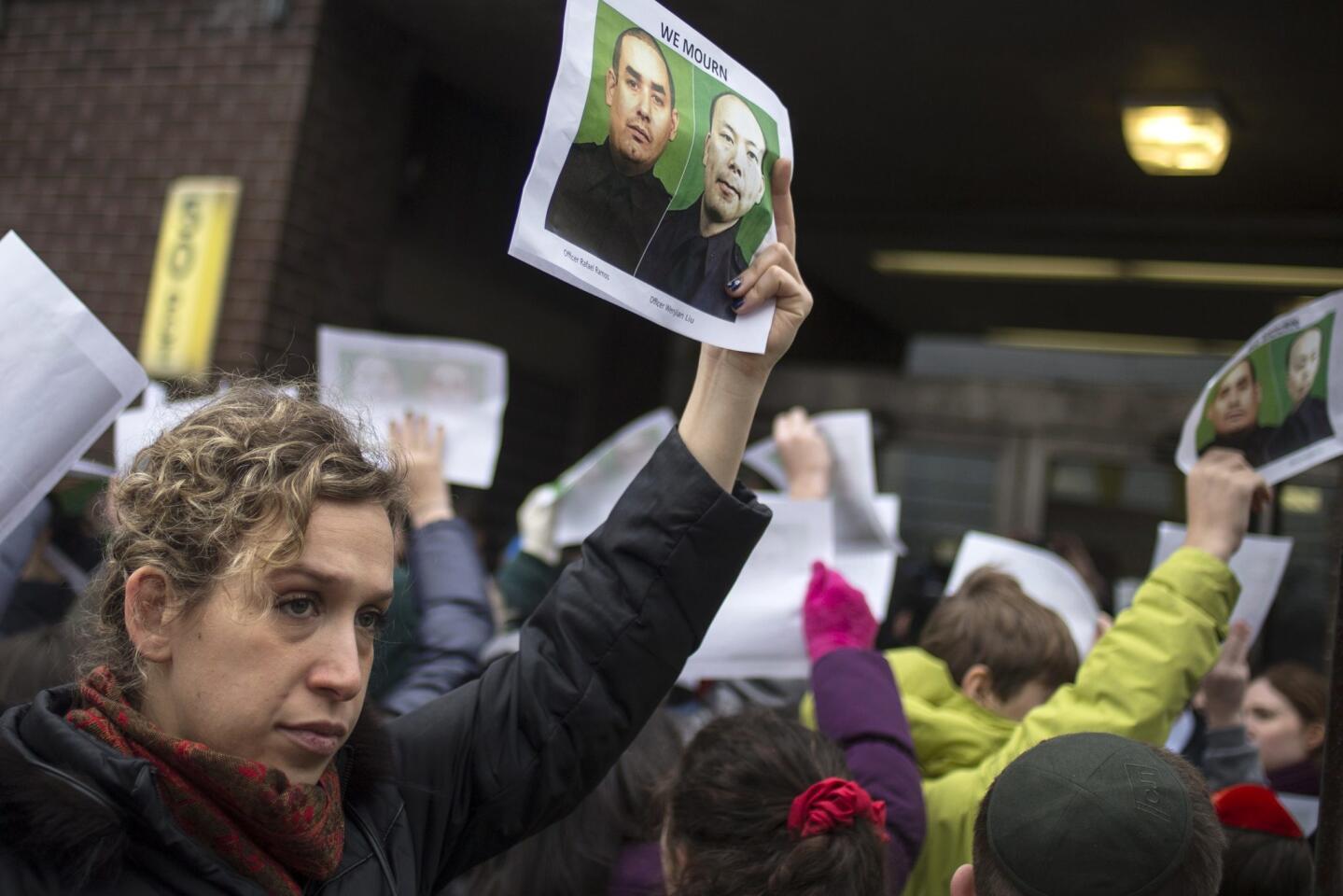 A woman holds images of slain New York Police Department (NYPD) officers Wenjian Liu and Rafael Ramos, who were shot and killed as they sat in a marked squad car in Brooklyn on Saturday, in New York