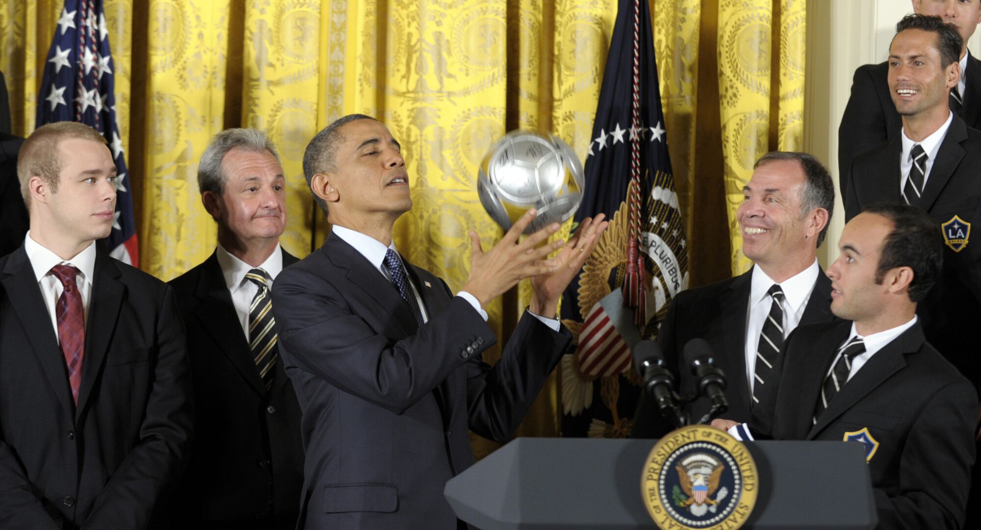 President Barack Obama catches a soccer ball after bouncing it off of his head as Galaxy coach Bruce Arena watches
