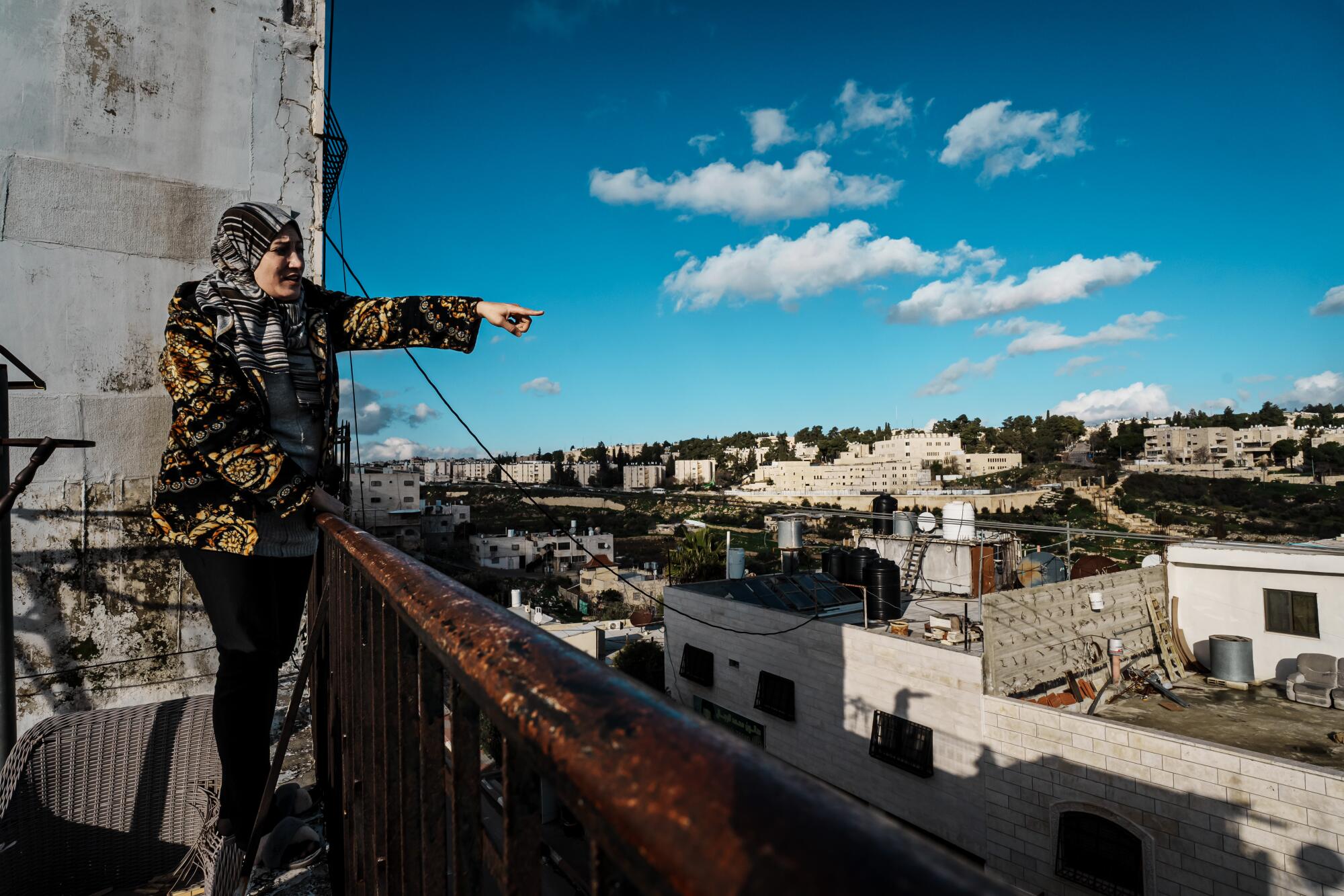 A woman in a headscarf pointing over the buildings below from her vantage point next to a metal railing