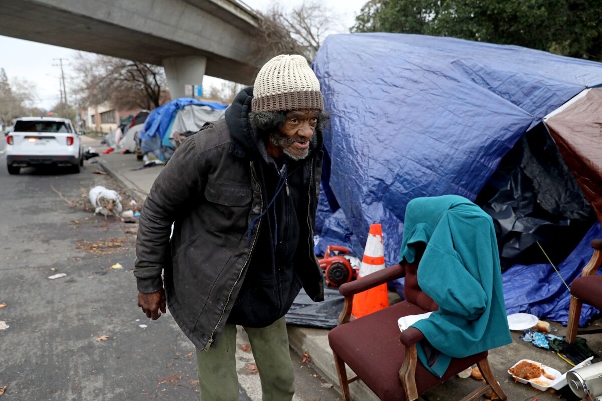 A person walks next to a sidewalk filled with tarps, chairs and other things.