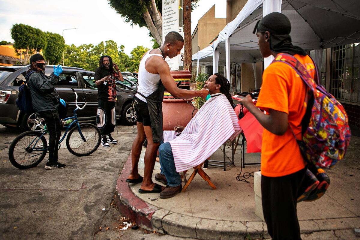 A street barber cuts a man's hair on the sidewalk.