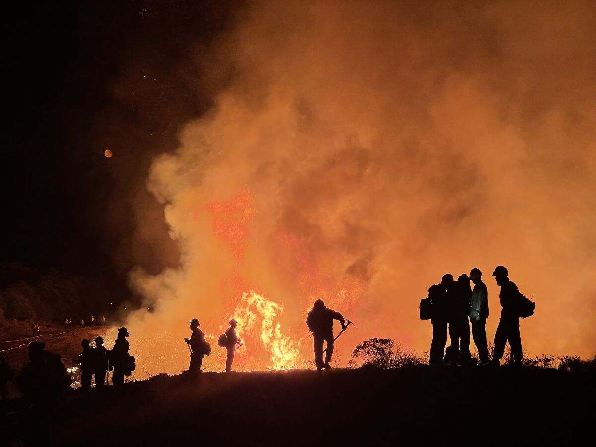 Firefighters silhouetted by fire and smoke