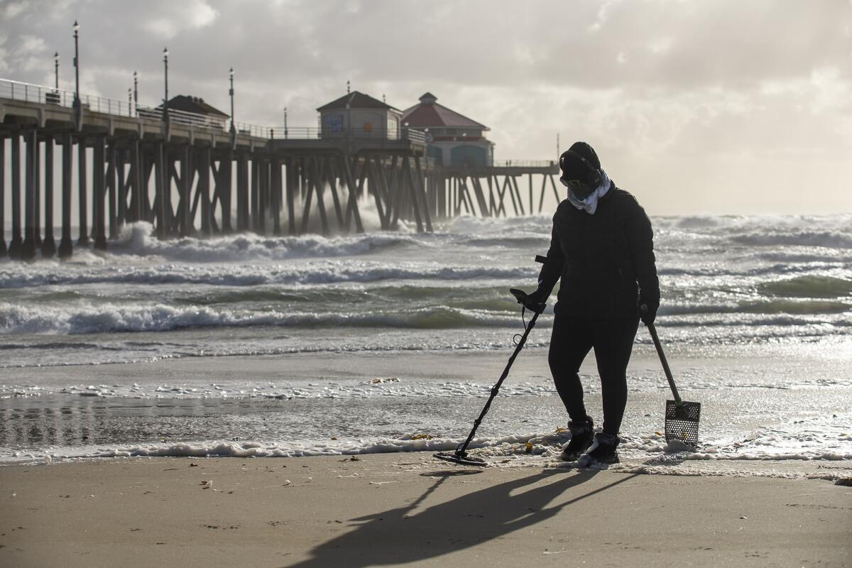 Irene Menzes searches for treasure with a metal detector near the Huntington Beach Pier on Monday, Jan. 25.