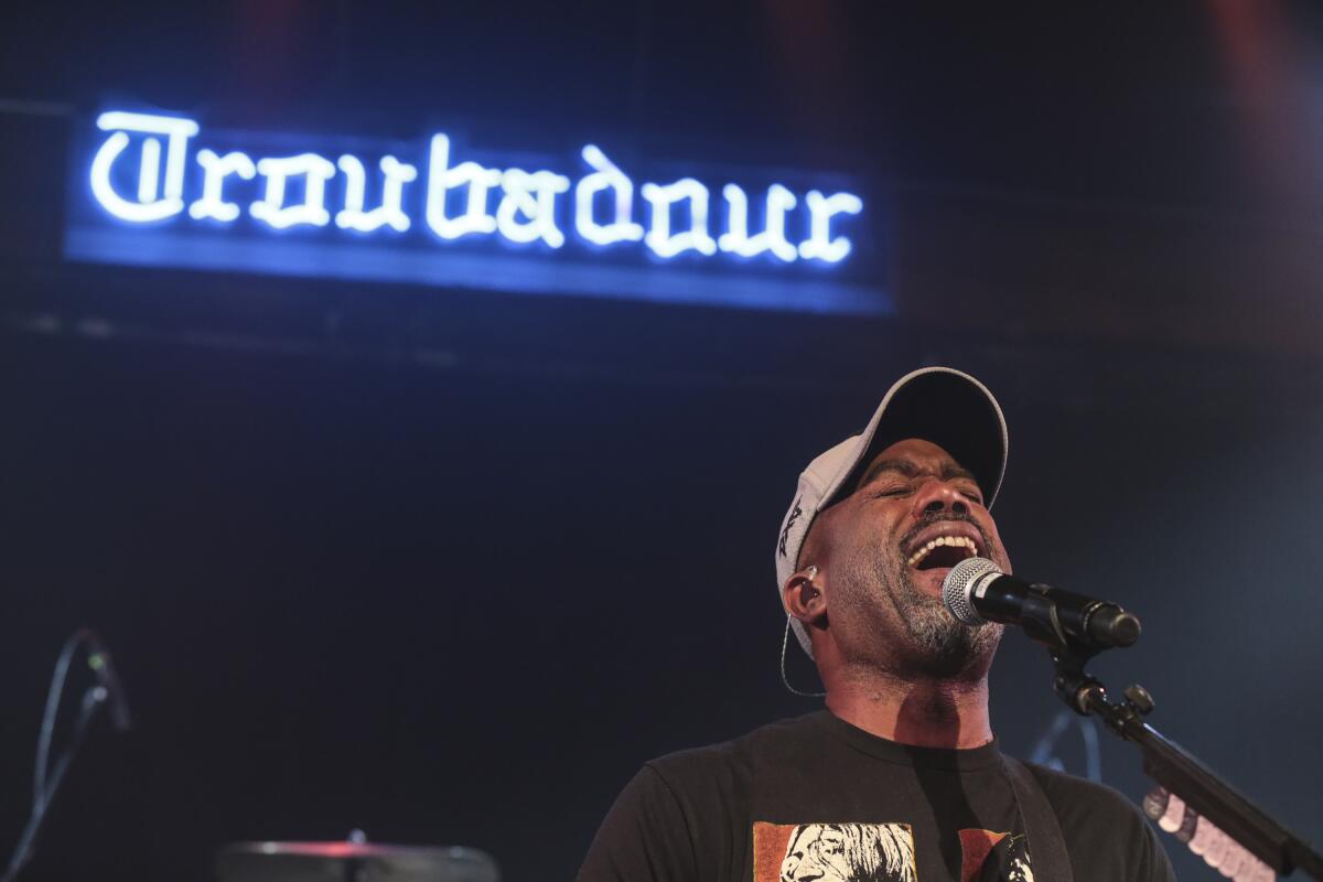 Darius Rucker sings with a blue neon "Troubador" sign above him.