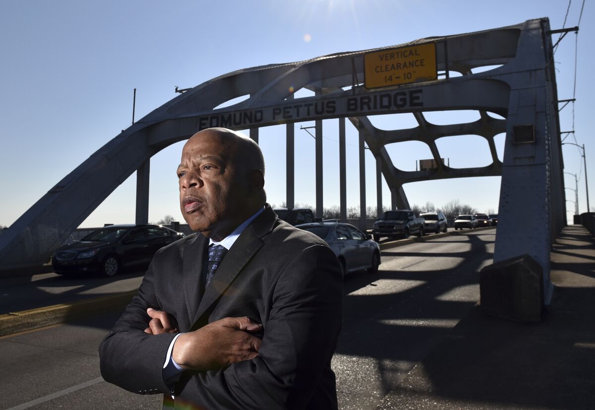 Rep. John Lewis stands in a dark suit with his arms crossed on the Edmund Pettus Bridge in Selma, Alabama
