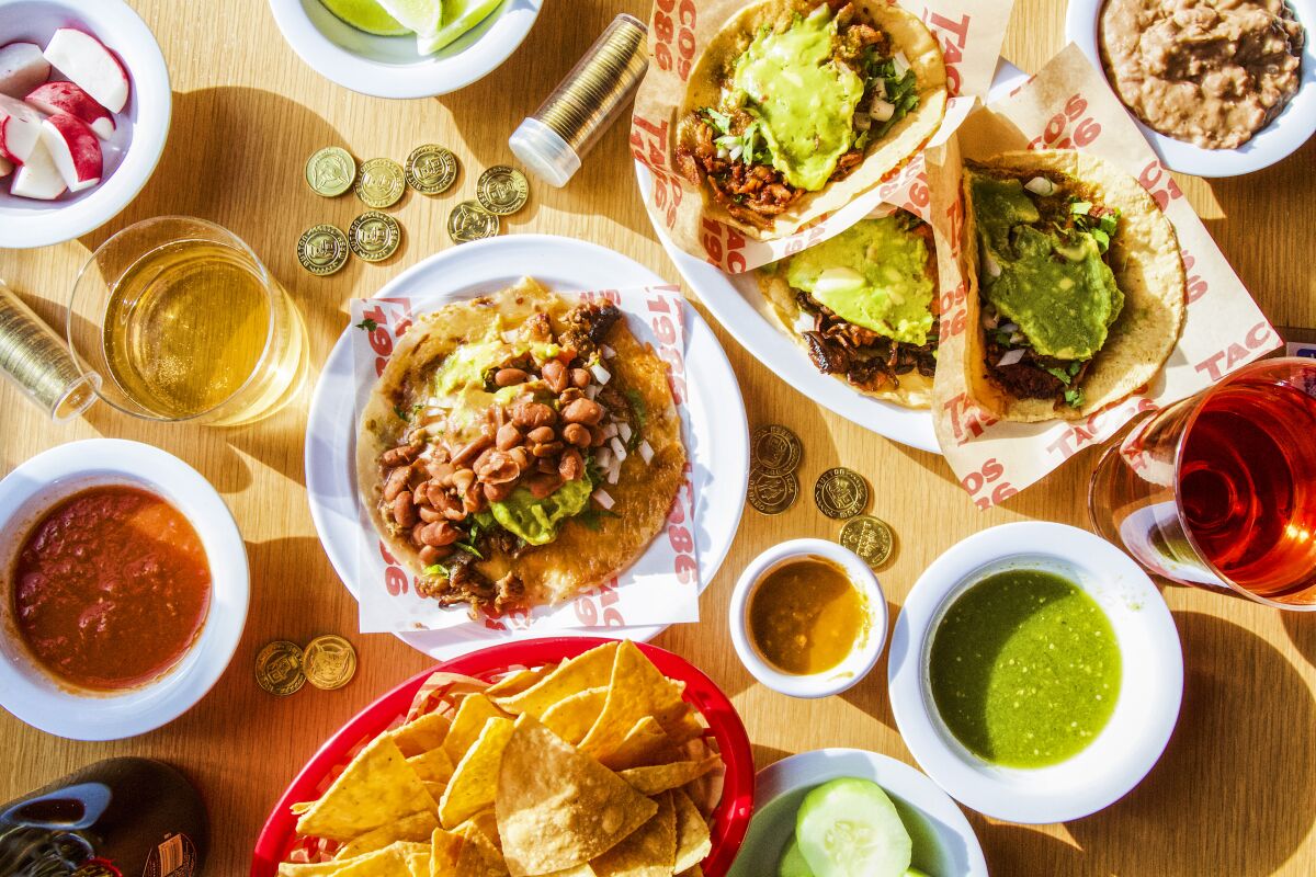 An overhead photo of a spread of Tacos 1986 tacos and salsas with Button Mash arcade tokens and wine.