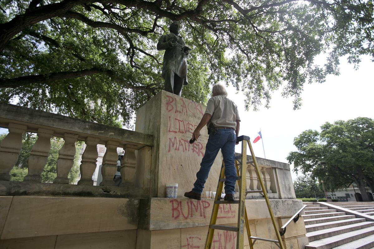 A university worker removes graffiti from a statue of Jefferson Davis on the south mall at the University of Texas in Austin.