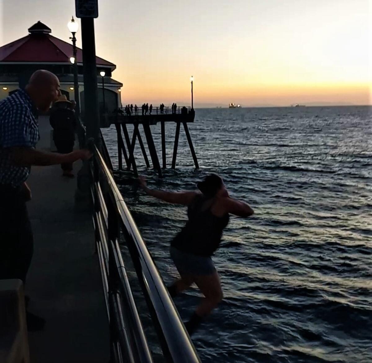 A woman jumps off a pier into the ocean as a man standing behind her shouts