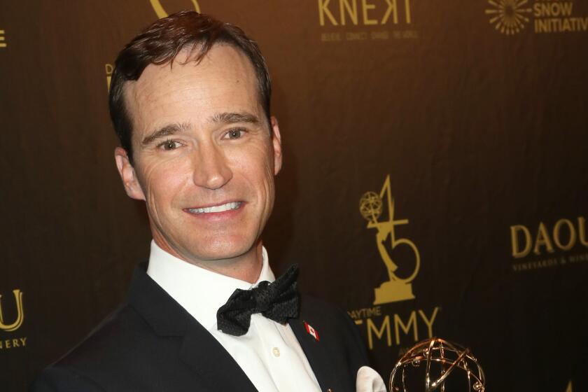 A man in a tuxedo holds an Emmy Award