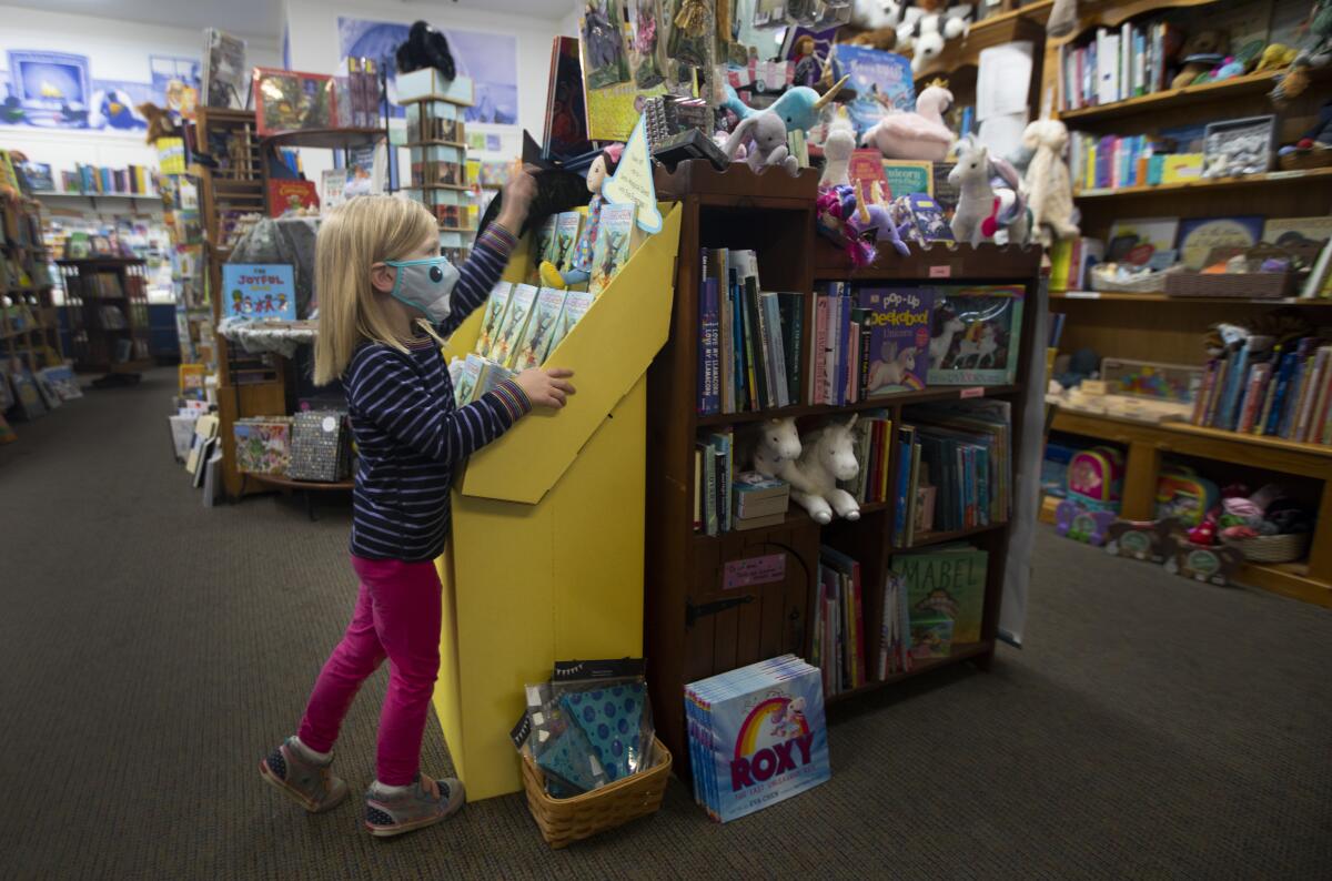 A girl in a mask looks at a yellow rack filled with books at Once Upon a Time bookstore.