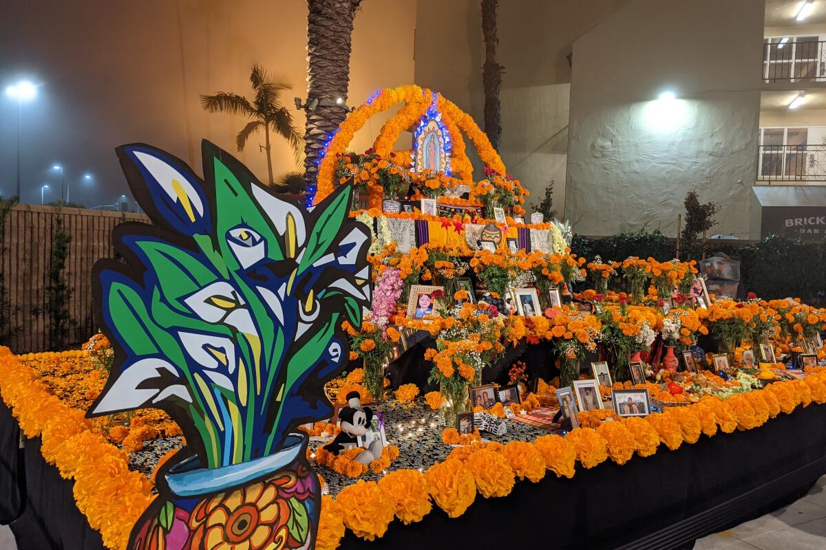 A community altar covered with orange marigolds and photos, with a large cutout of a pot of calla lillies.