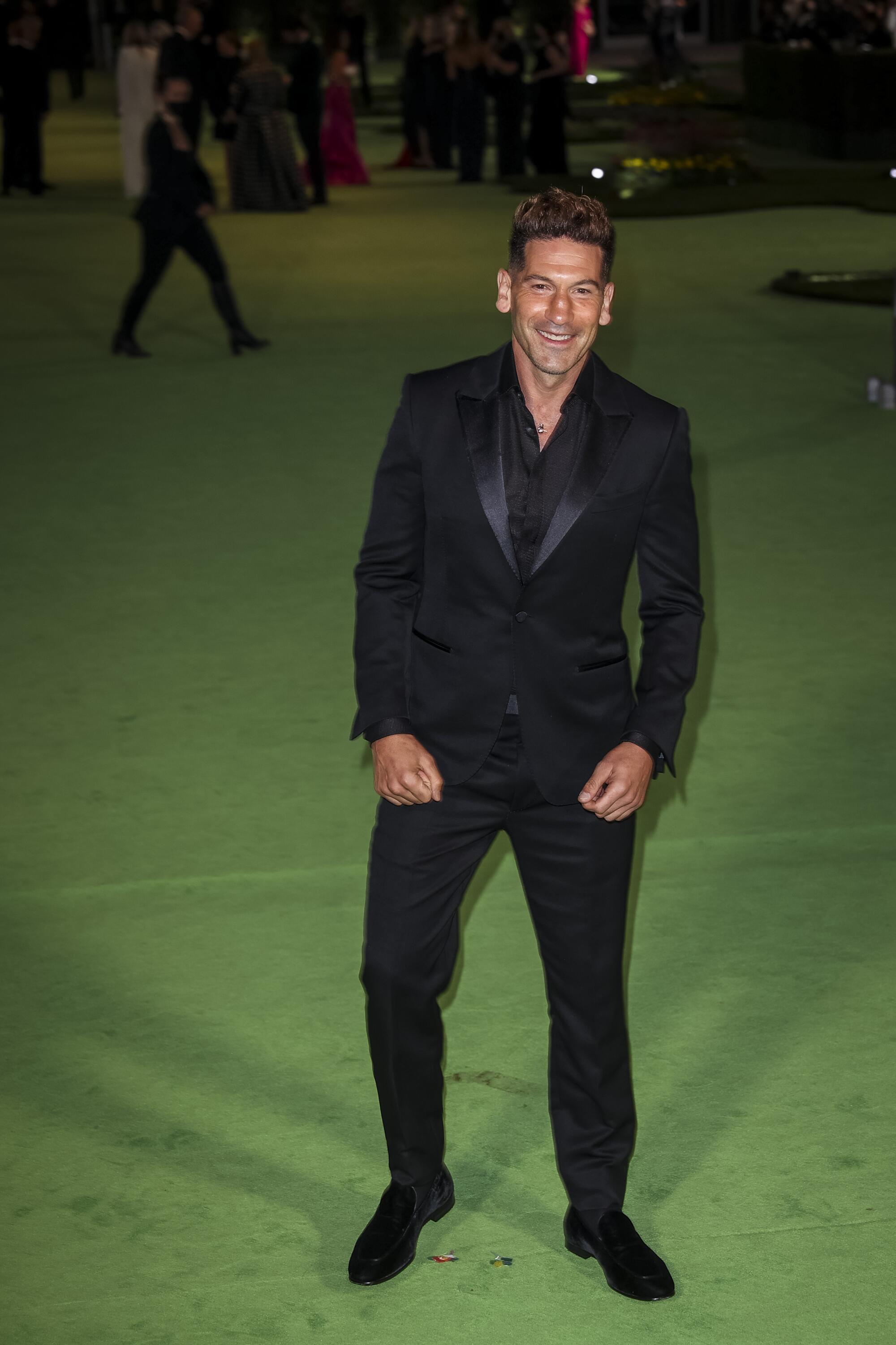 A man in a black suit posing on a green carpet