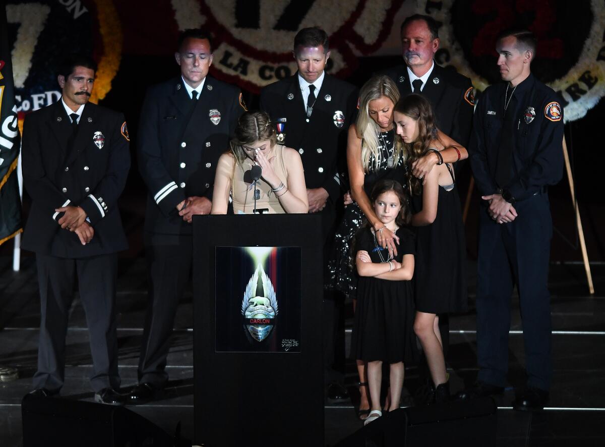 A girl speaks at a podium as her family and firefighters look on 