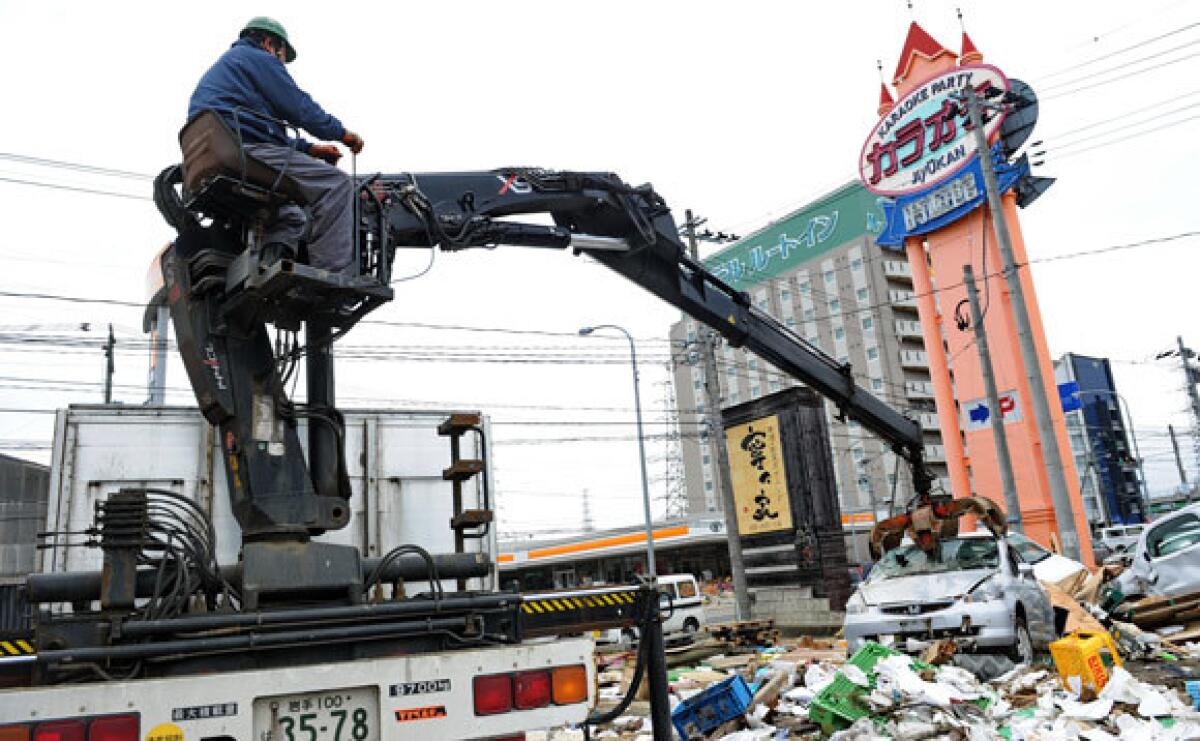 A worker lifts a destroyed car from a mound of debris in Sendai, Miyagi prefecture. The earthquake and tsunami generated an estimated 80 million tons of debris.