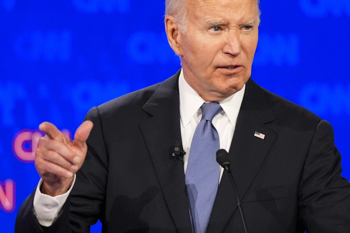 President Biden pointing and speaking against a royal-blue backdrop
