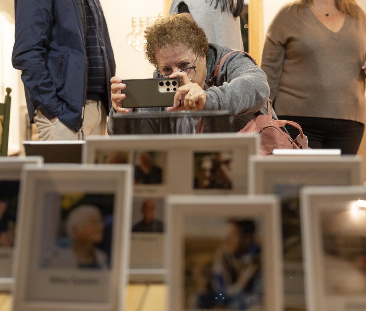 બત્યા હોલિન ફોટોગ્રાફ્સ એક ઘરમાં પ્રદર્શનમાં લોકોના ચિત્રો ફ્રેમ કરે છે.