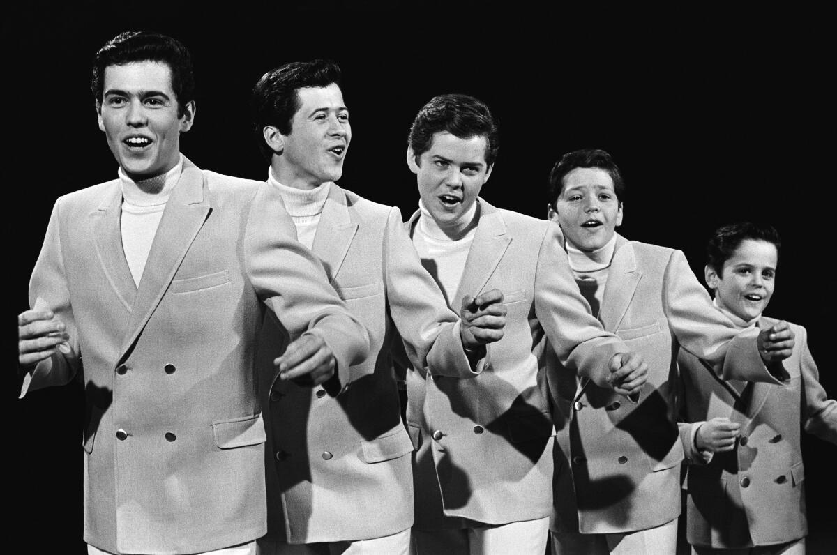 Five Osmond brothers of different ages, arranged from tall to short, dressed in suits in a black and white photograph.
