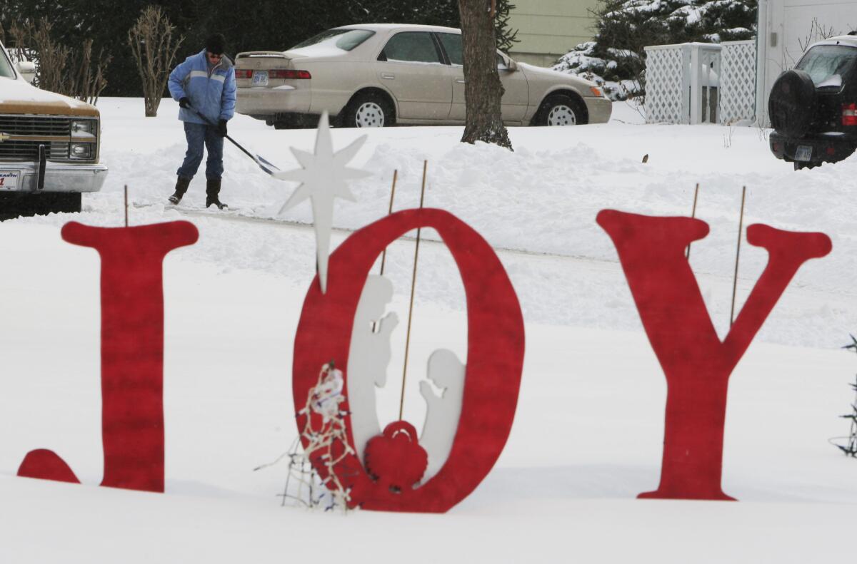 The word "joy" in large red letters stands in a snow-covered yard as a person shovels a walkway in the background