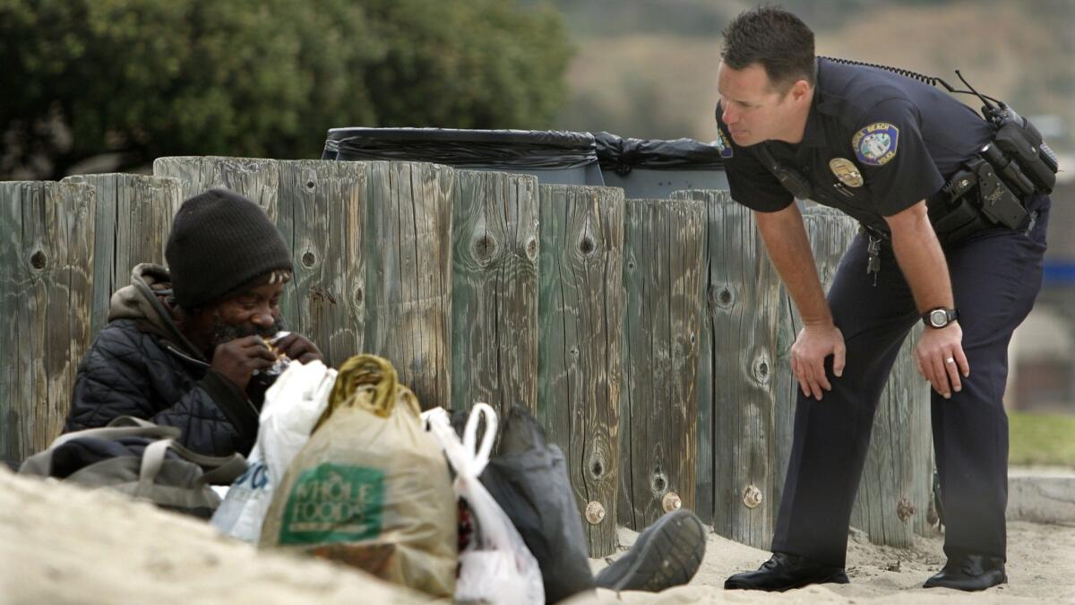 A Laguna Beach police officer talks with a homeless man at Main Beach in this file photo. Laguna and the American Civil Liberties Union reached a settlement this week in a 2015 lawsuit alleging Americans with Disabilities Act violations at the city’s night homeless shelter.