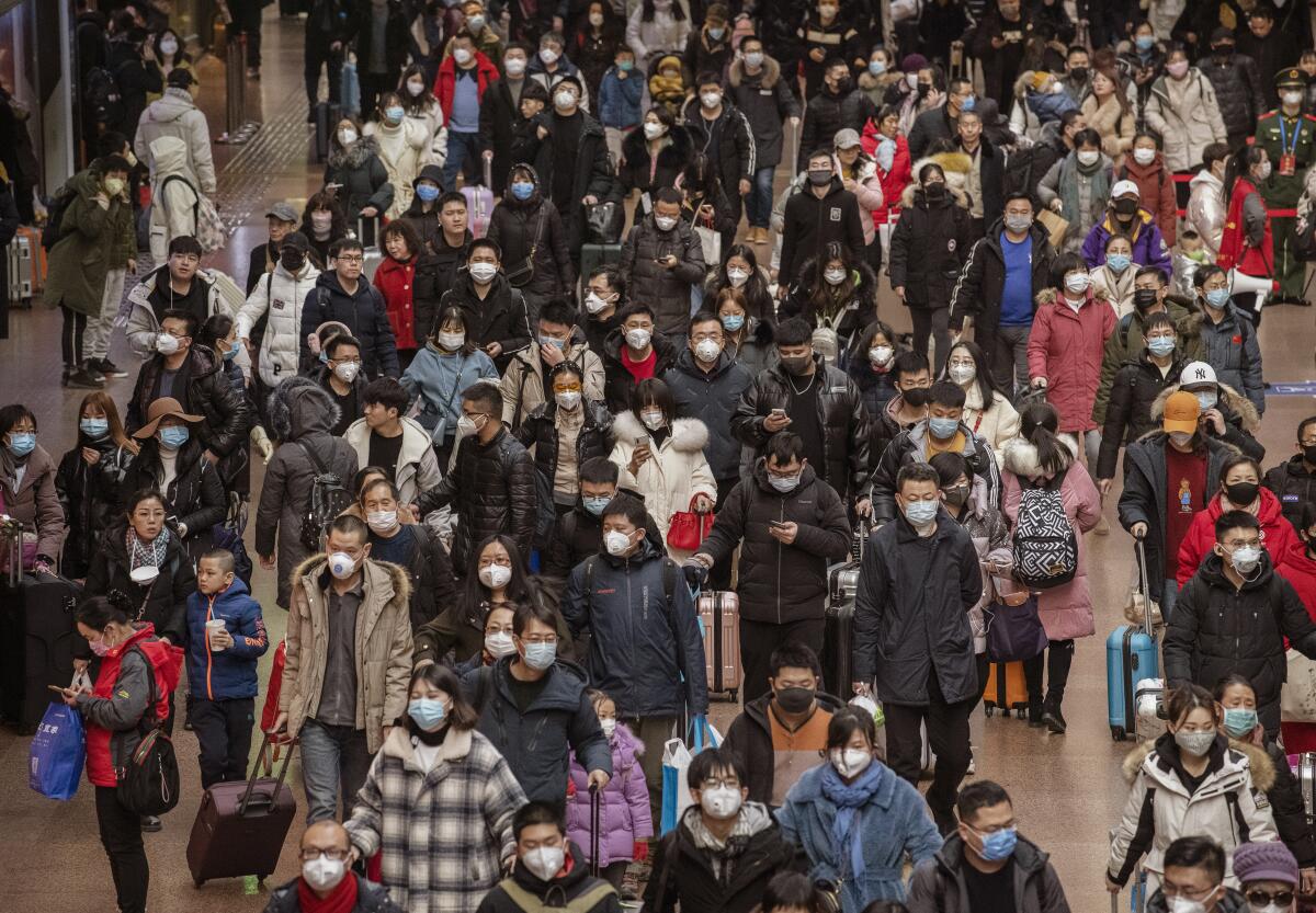 Chinese travelers, most wearing masks, arrive to board trains before the annual Spring Festival at a Beijing railway station.