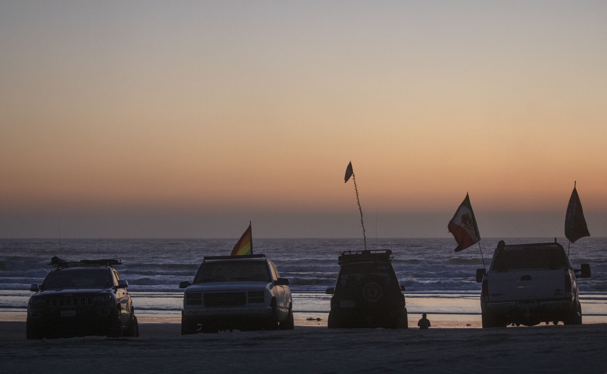 Trucks sporting flags parked on the beach with the ocean behind