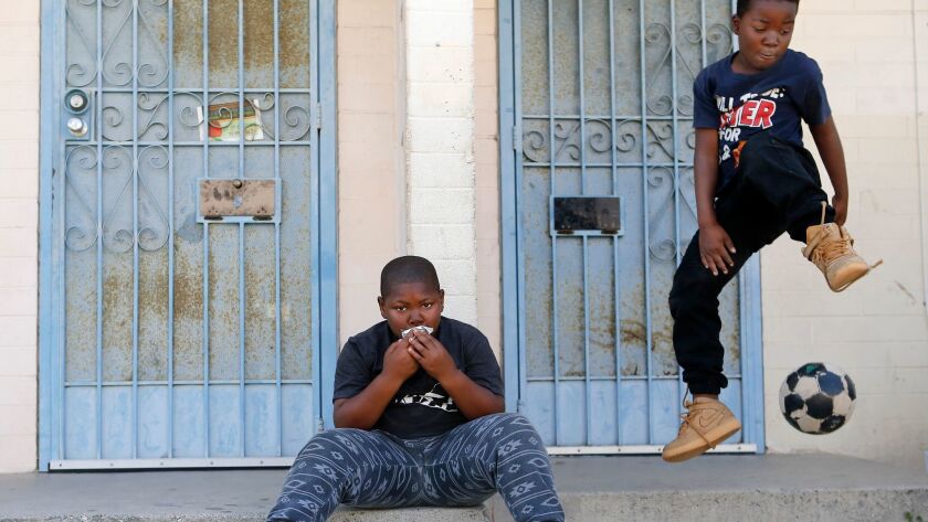 Demarion Washington, 8, left, drinks juice in front of his home as Justin Scott, 8, leaps from a porch at the Jordan Downs Housing Projects in Watts, Calif. on June 5.