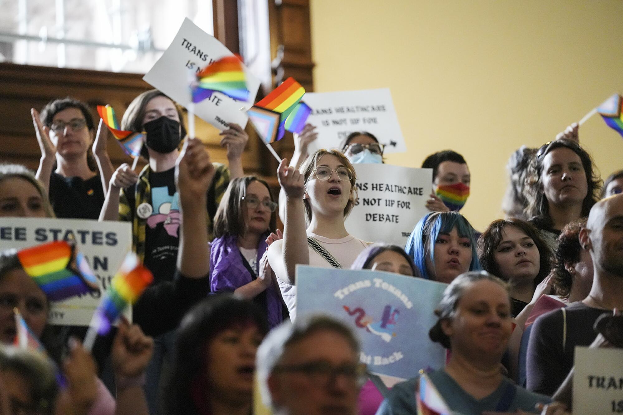 Activists hold signs and rainbow flags in the Texas Capitol.