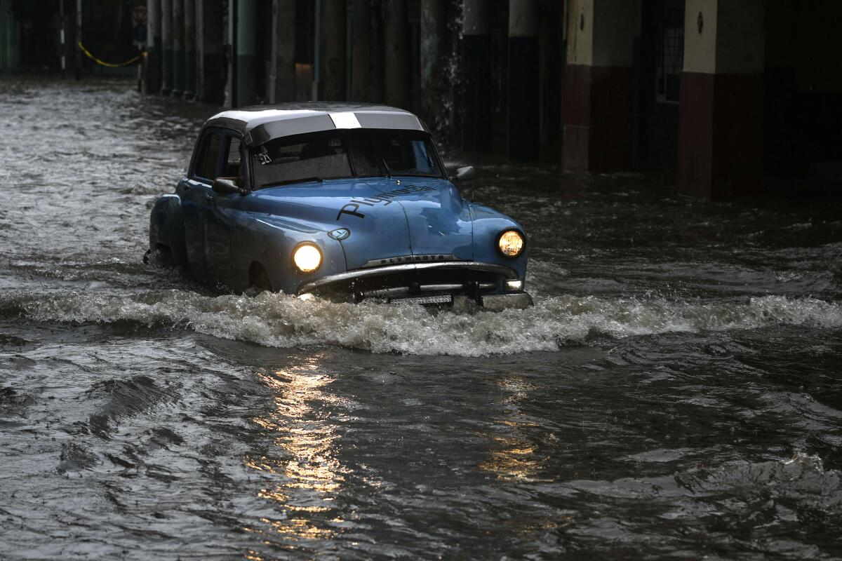 Una persona conduce un automóvil clásico estadounidense por una calle inundada por fuertes lluvias, 