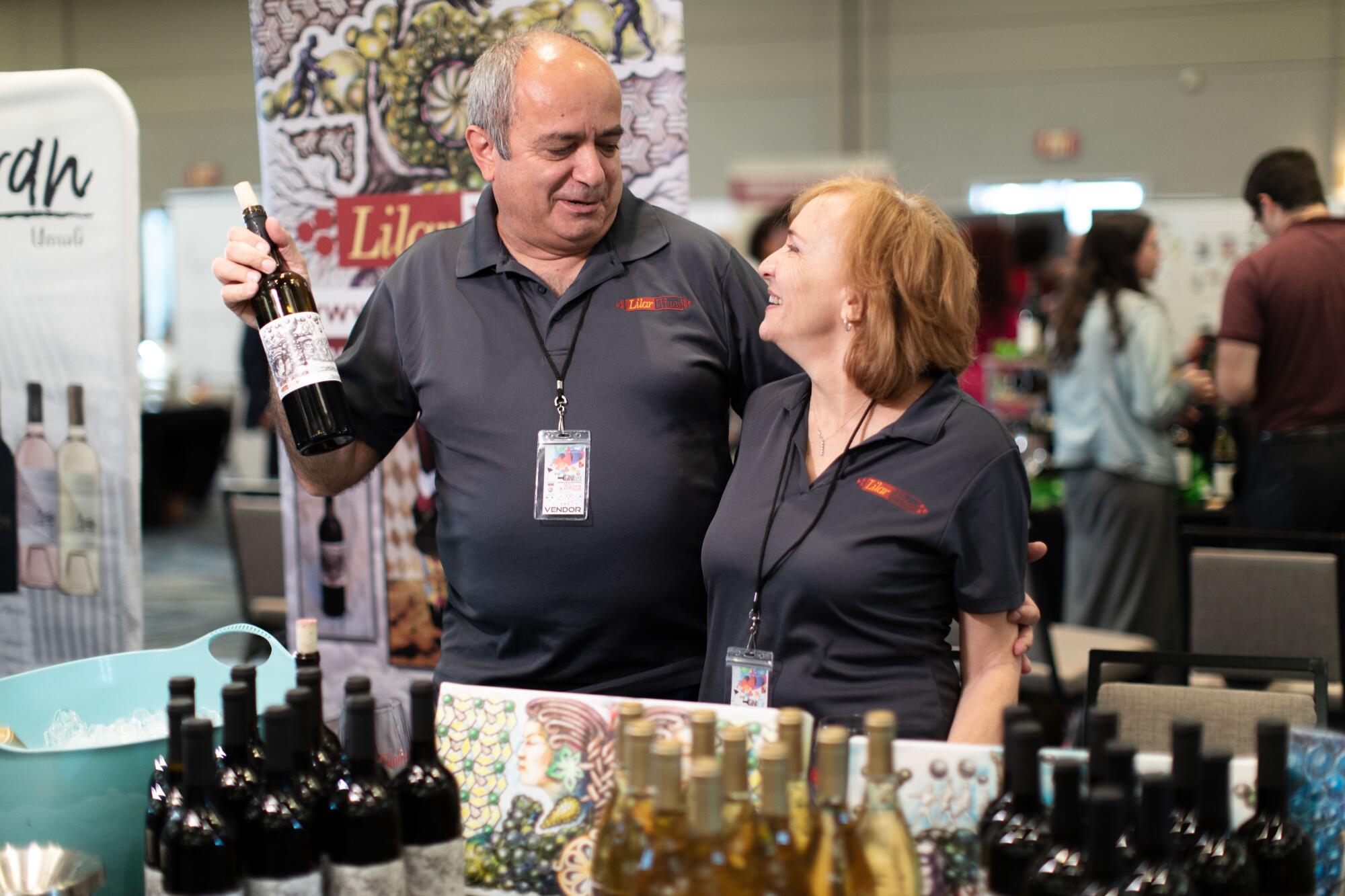 A man and woman stand looking at each other behind a table displaying bottles of wine.