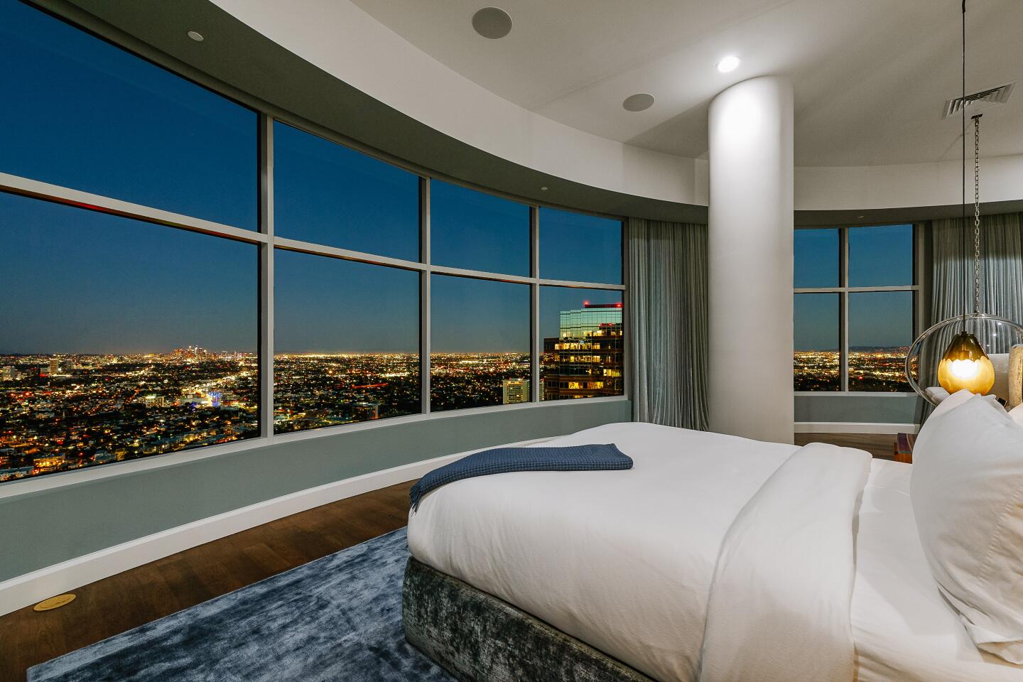 A bed is surrounded by large windows.