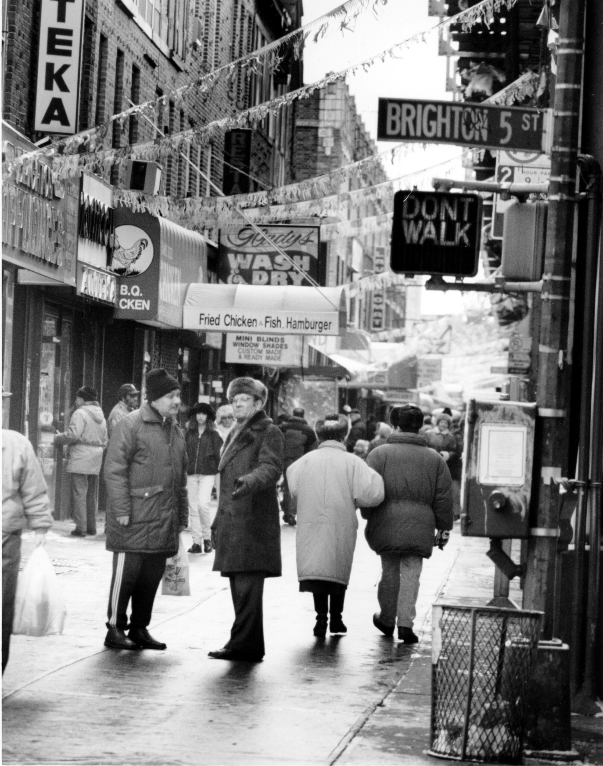 A black-and-white photo of people in coats and fur hats walking on the street.