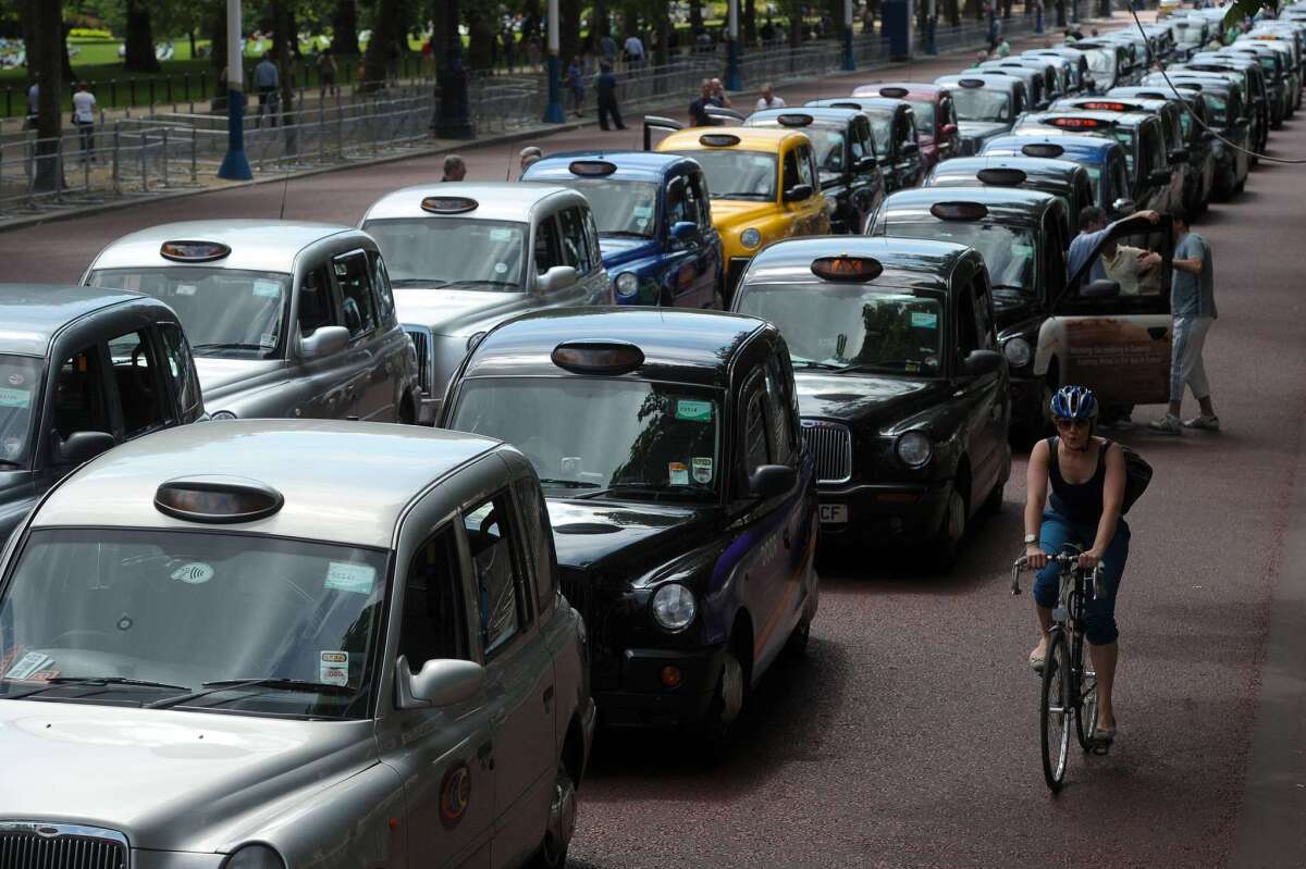 A cyclist rides past parked taxis during a protest by London black cab drivers against new private taxi service Uber, a mobile phone app, on the Mall leading to Buckingham Palace in central London on Wednesday.