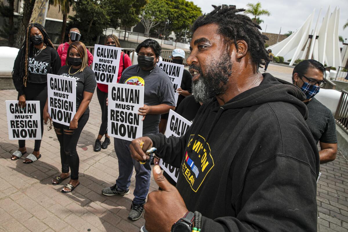 A man speaks at a news conference as people stand in protest at Compton City Hall.