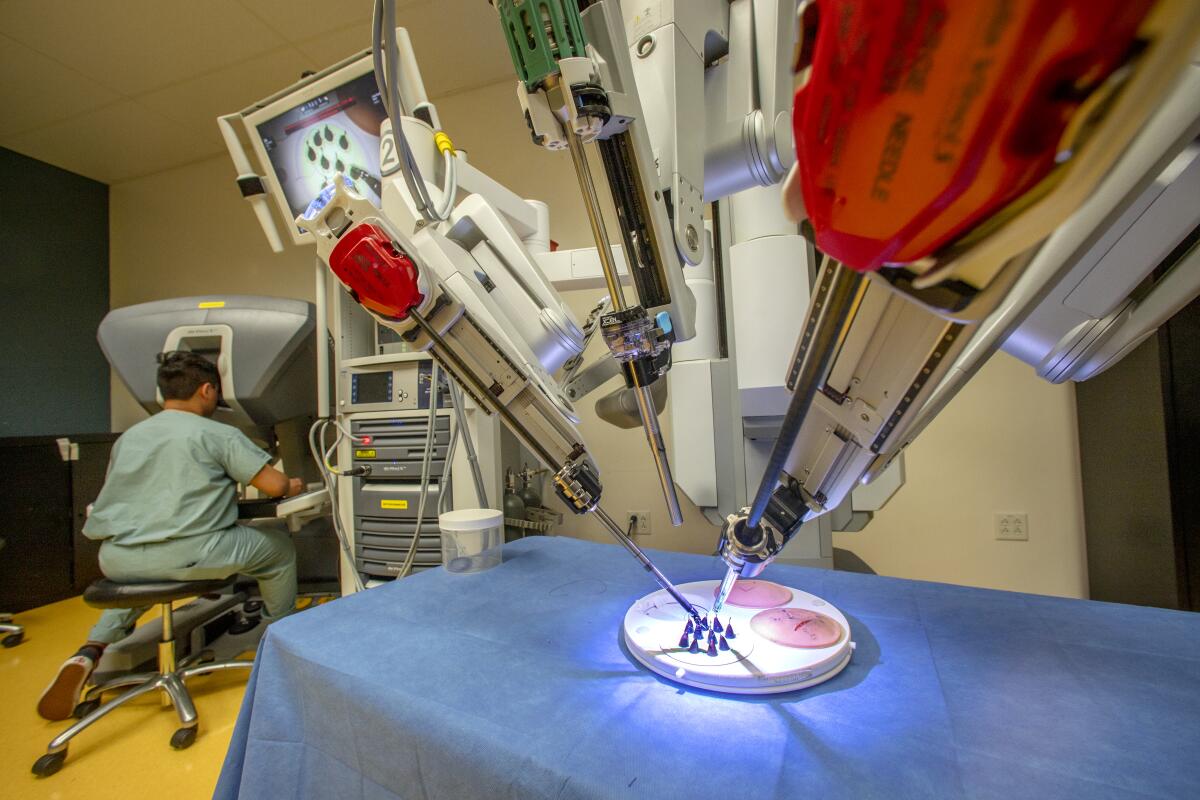 A student uses a console to control a daVinci Surgical System robot, which performs complex surgical procedures with a minimally invasive approach.