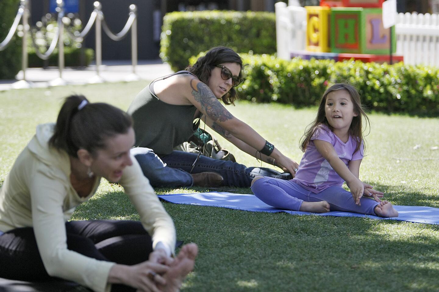 Kala Fernandez, 4 of Glendale, right, and her mom Vivian Fernandez, center, follow instructor Michele Kackovic's instructions in the children's Yoga class on the lawn at the Americana at Brand in Glendale on Wednesday, April 10, 2013. The class began today and will continue once per week until further notice, according to instructor Kackovic.