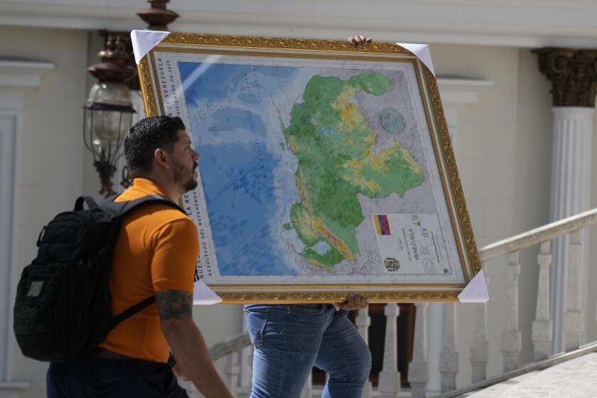 A man carries the new map of Venezuela with the Essequibo territory, a large swath of land that is administered and controlled by Guyana but claimed by Venezuela, to the National Assembly building in Caracas, Venezuela, Wednesday, Dec. 6, 2023. (AP Photo/Ariana Cubillos)