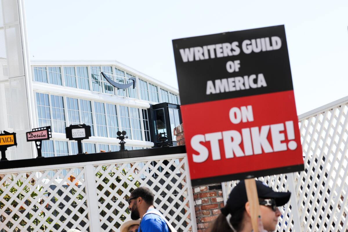 A person holds a strike sign outside a studio with the Amazon logo