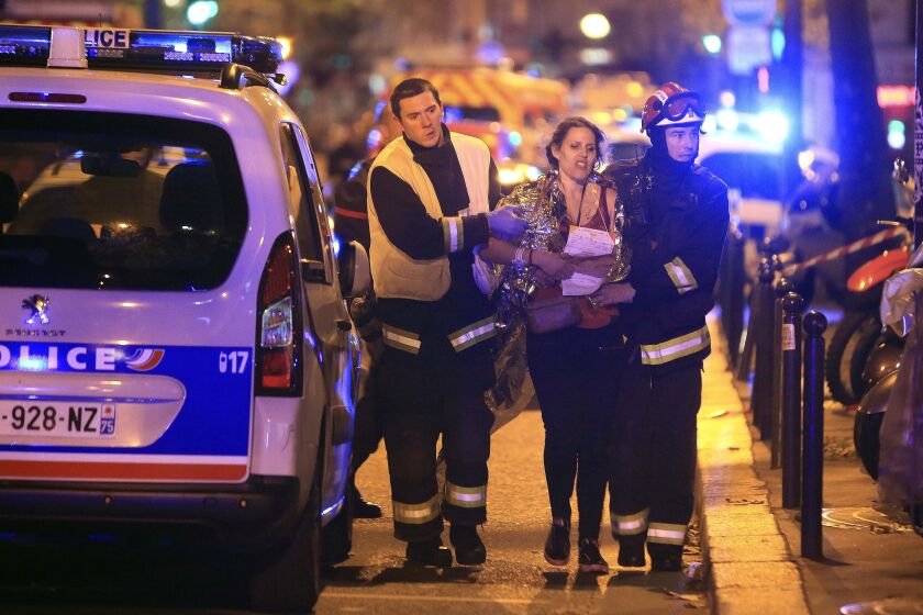 FILE - In this Nov. 13, 2015, file photo, rescue workers help a woman after an attack by Islamic State militants, outside the Bataclan theater in Paris. On Nov. 13, 2015, a cell of nine Islamic State militants armed with automatic rifles and explosive vests left a trail of dead and injured at the national stadium, Paris bars and restaurants and the Bataclan concert hall. Nearly all the attackers were from France or Belgium, as were the cell's 10th member — the only one still alive. He is the chief defendant among 20 people charged in a trial that is expected to last nine months. (AP Photo/Thibault Camus, File)