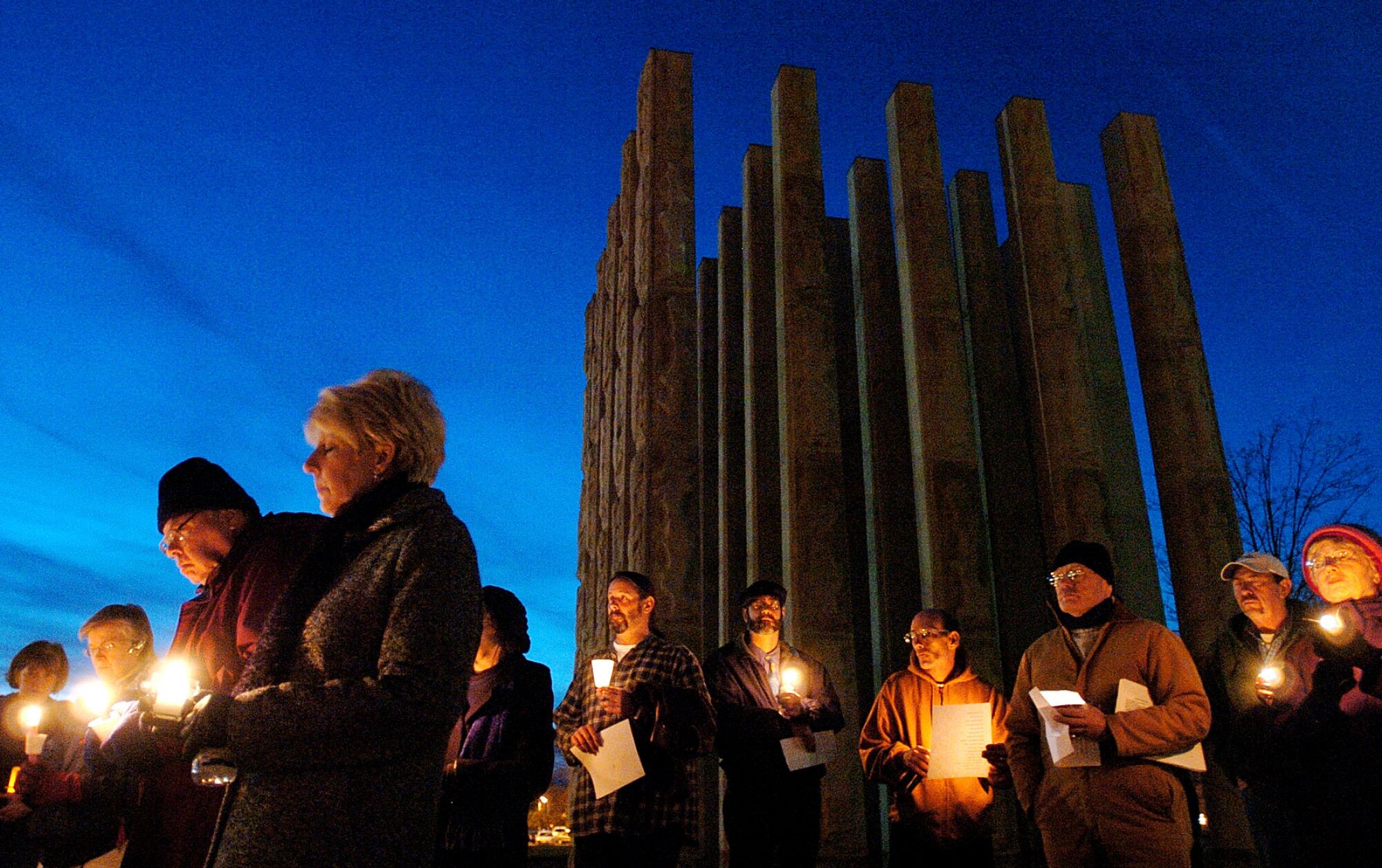 People hold candles in the dark at a vigil as the Bartholomew County Memorial for Veterans looms behind them.