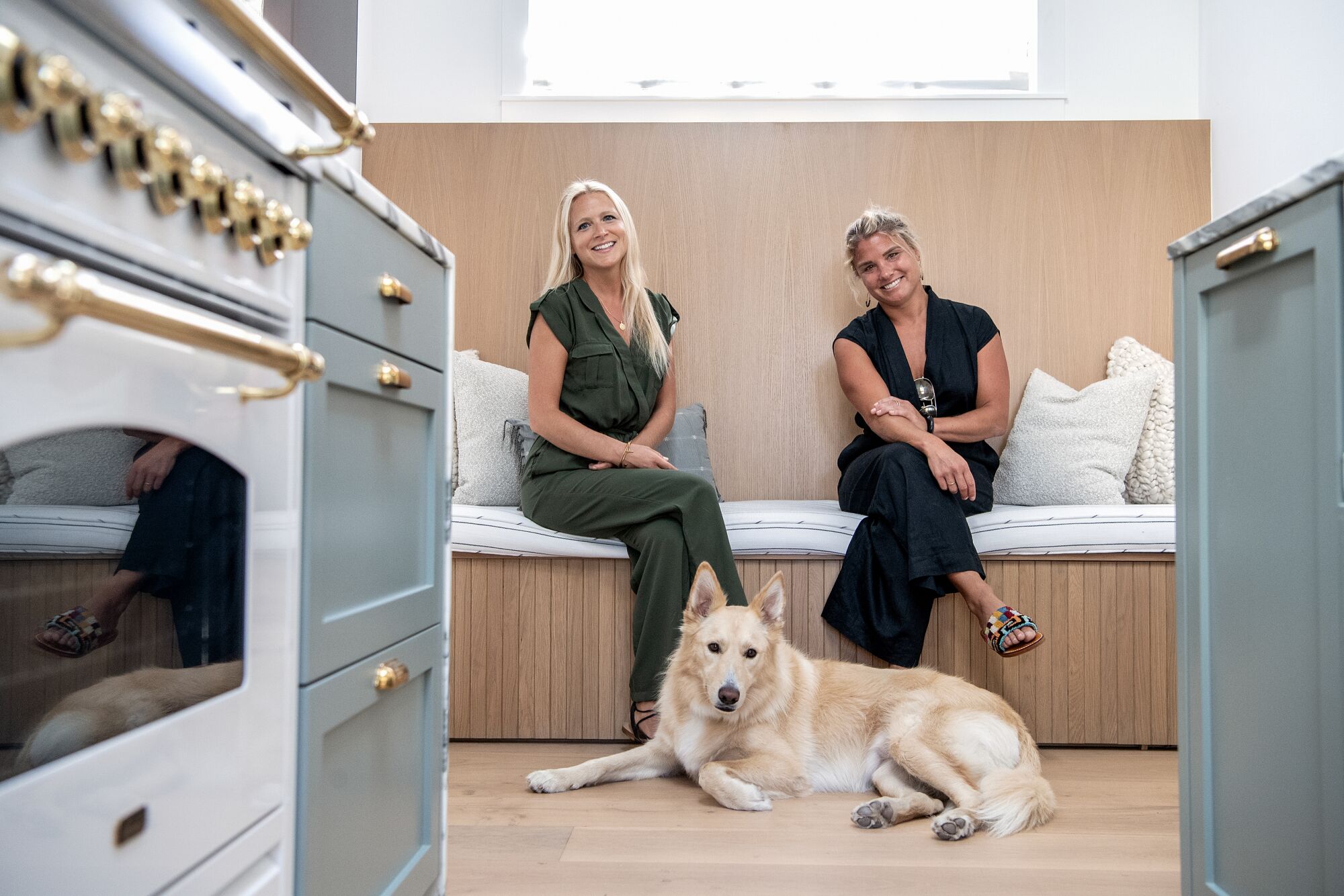 Designers Kristen Gundersen and Jenna Richter sit on a banquette with a dog 