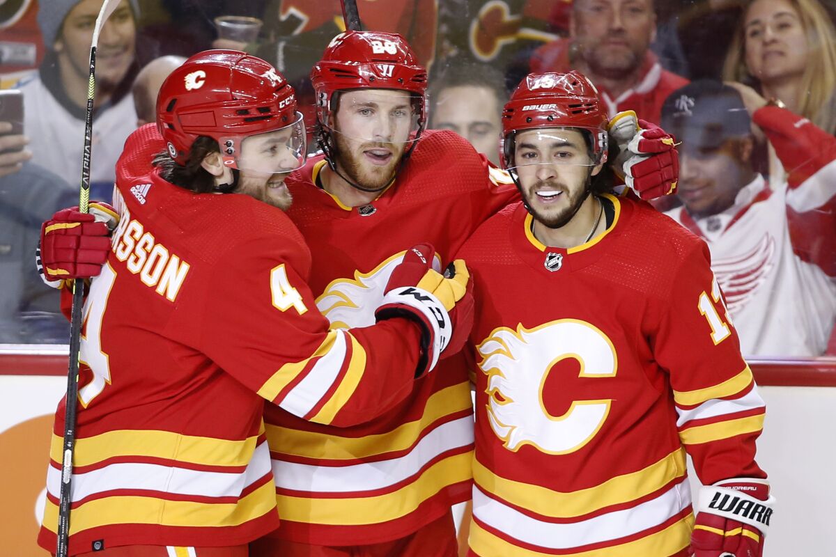 Calgary Flames center Elias Lindholm (28) celebrates his goal with teammates Rasmus Andersson, left, and Johnny Gaudreau against the Detroit Red Wings during the first period of an NHL hockey game Saturday, March 12, 2022 in Calgary, Alberta. (Larry MacDougal/The Canadian Press via AP)