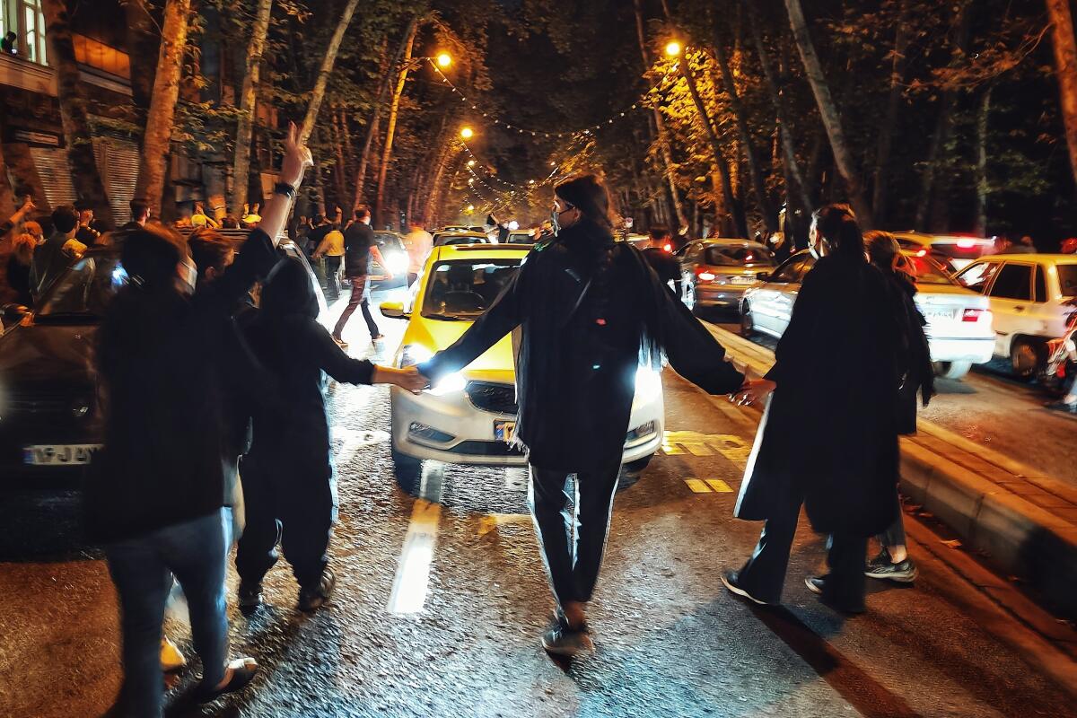 Iranians in Tehran protest by holding hands in front of traffic at night.