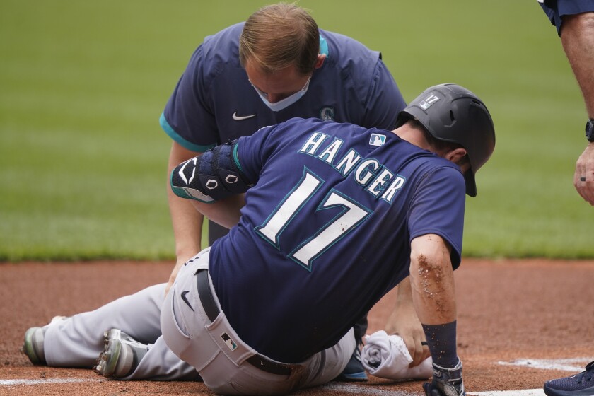 A trainer looks at Seattle Mariners' Mitch Haniger after Haniger was hit by a pitch in the first inning of a baseball game against the Cleveland Indians, Sunday, June 13, 2021, in Cleveland. Haniger left the game after the incident. (AP Photo/Tony Dejak)