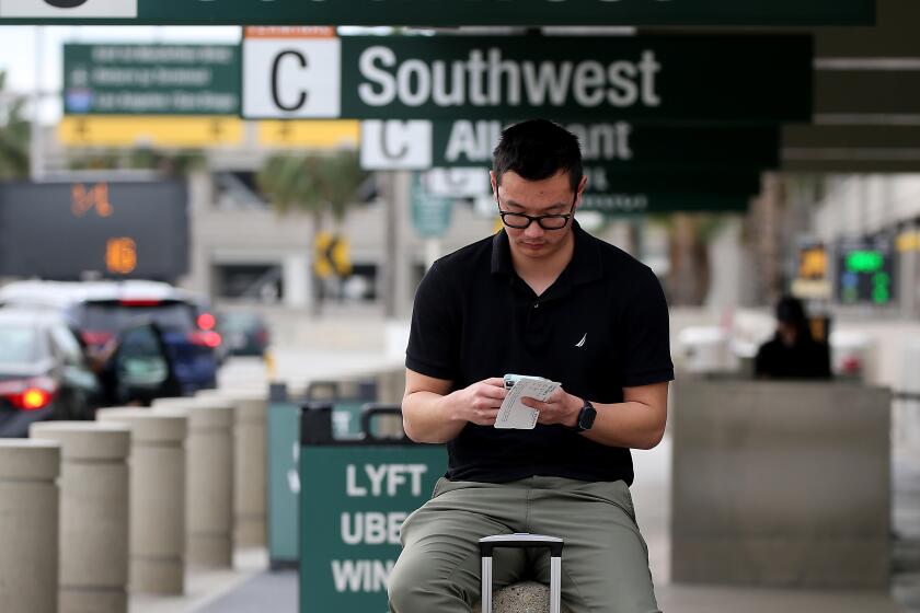 SANTA ANA, CALIF. - DEC. 27, 2022. Kenneth Zhou waits for a ride at John Wayne Airport on Tuesday, Dec. 27, 2022, after a three-day journey from Phoenix because of delays, layovers and cancelations by Southwest Airlines. The budget carrier has canceled thousands of flights over the Christmas holidays . (Luis Sinco / Los Angeles Times)