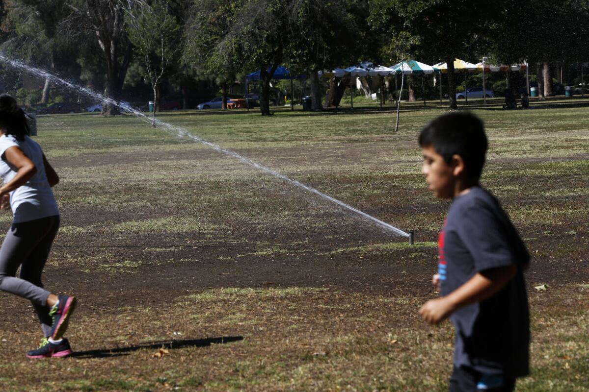 Two children run past sprinklers at Warner Ranch Park in the San Fernando Valley in June. New reports show Angelenos cut water use by 21% in July.