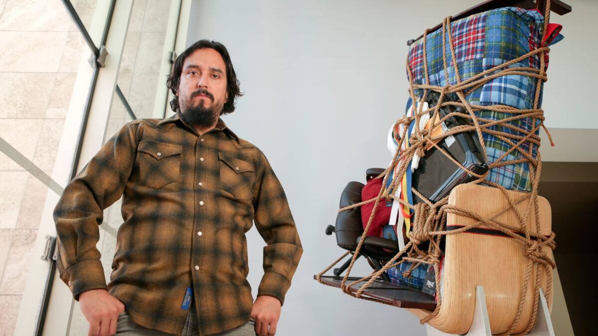 Camilo Ontiveros stands before "Temporary Storage," made from the belongings of a DACA deportee, on display at LACMA. (Irfan Khan / Los Angeles Times)